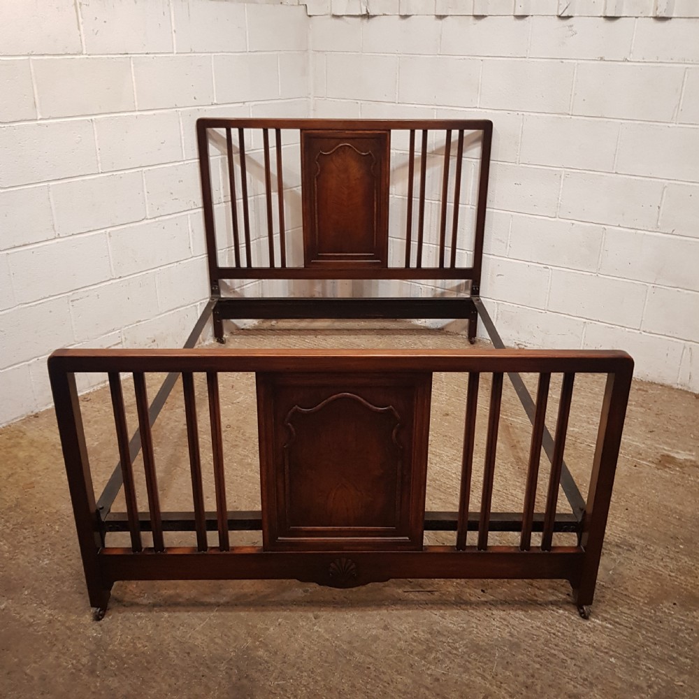 An antique dark walnut double bedstead featuring a central arched panel flanked by vertical slats on both the headboard and footboard, set with metal side rails.