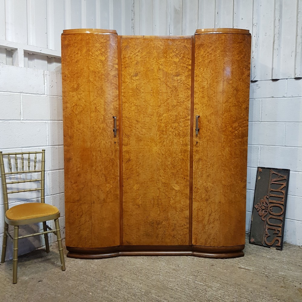 An Art Deco triple wardrobe crafted from highly figured burr walnut featuring curved outer doors and vertical metal handles.