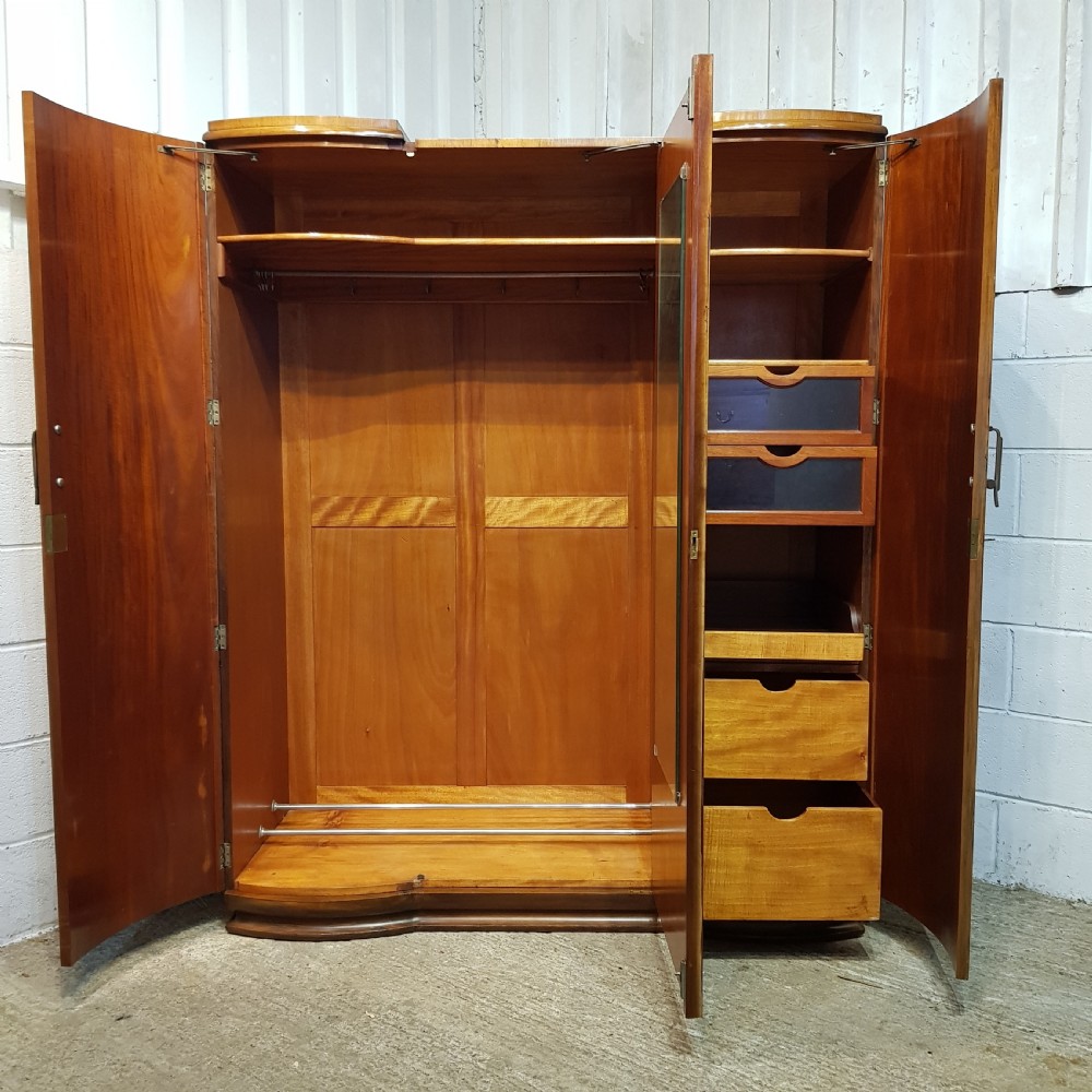 An Art Deco triple wardrobe crafted from highly figured burr walnut featuring curved outer doors and vertical metal handles. View VI