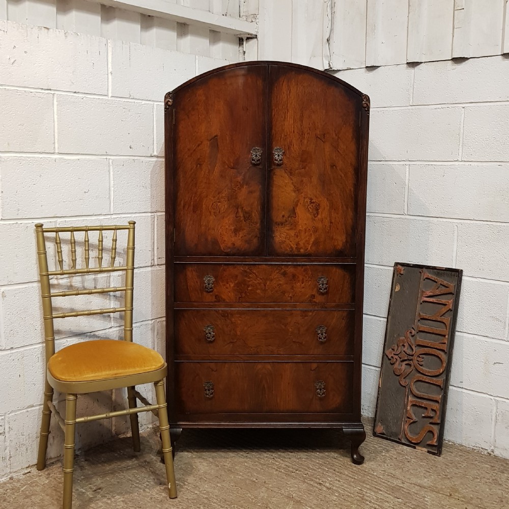 A 1920s burr walnut tallboy featuring an arched top two-door cabinet over three wide drawers with ornamental brass handles and cabriole feet.