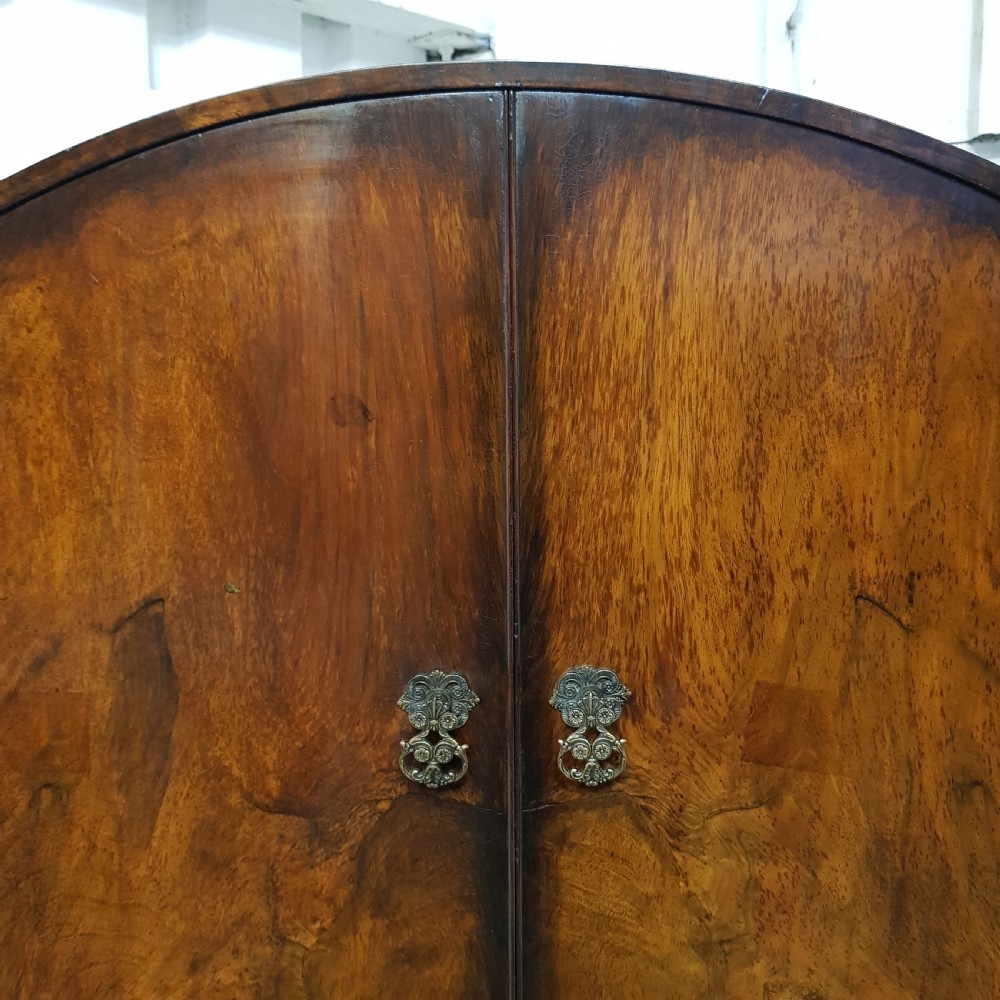 A 1920s burr walnut tallboy featuring an arched top two-door cabinet over three wide drawers with ornamental brass handles and cabriole feet. View III