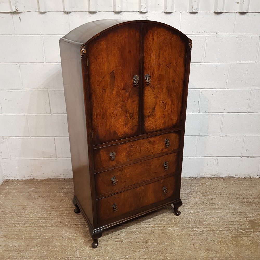 A 1920s burr walnut tallboy featuring an arched top two-door cabinet over three wide drawers with ornamental brass handles and cabriole feet. View VII