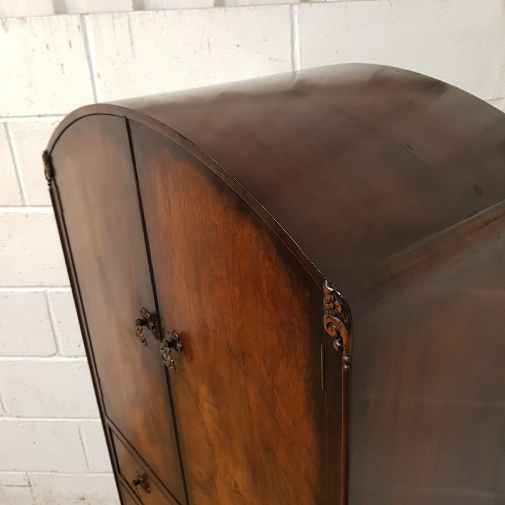 A 1920s burr walnut tallboy featuring an arched top two-door cabinet over three wide drawers with ornamental brass handles and cabriole feet. View VIII