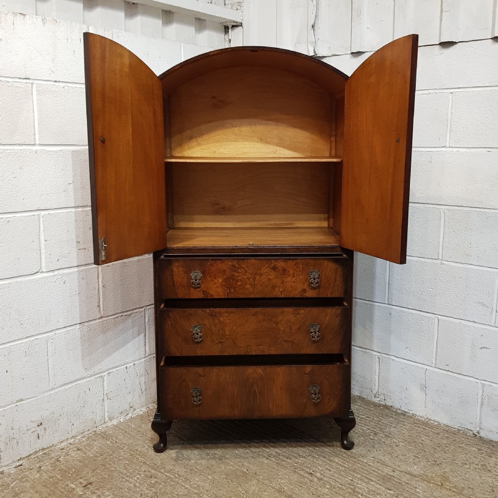 A 1920s burr walnut tallboy featuring an arched top two-door cabinet over three wide drawers with ornamental brass handles and cabriole feet. View IX