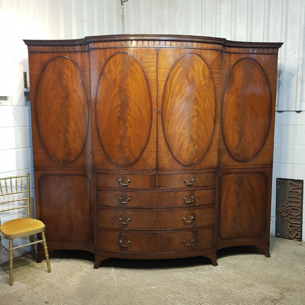 A large mahogany breakfront triple wardrobe featuring oval flame mahogany veneer panels on the doors and a central chest of drawers.