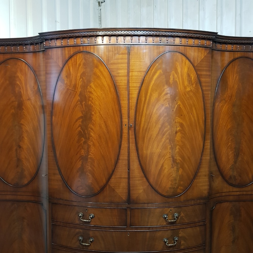 A large mahogany breakfront triple wardrobe featuring oval flame mahogany veneer panels on the doors and a central chest of drawers. View V