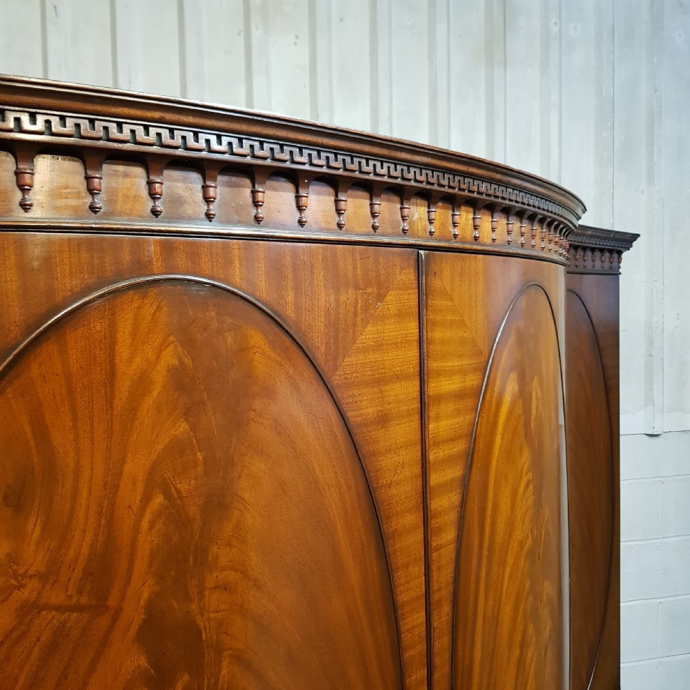A large mahogany breakfront triple wardrobe featuring oval flame mahogany veneer panels on the doors and a central chest of drawers. View VIII