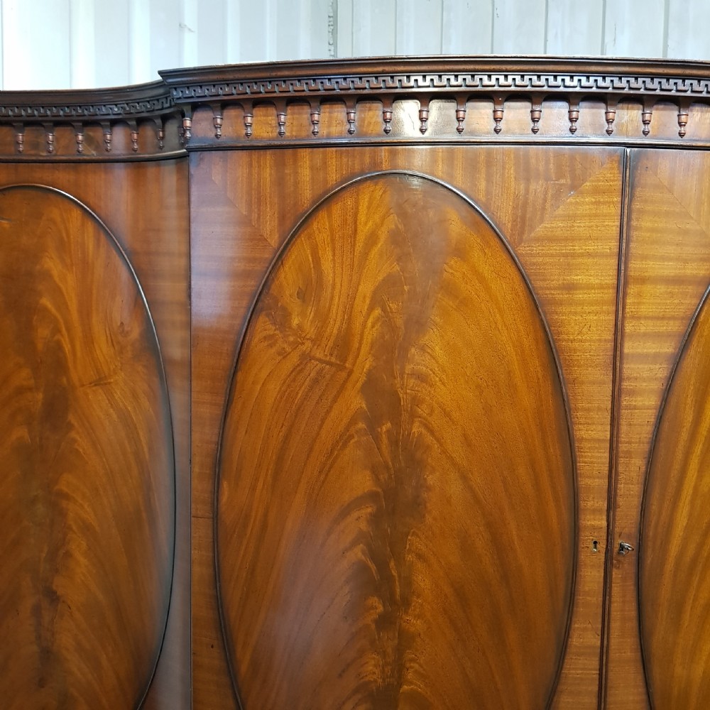 A large mahogany breakfront triple wardrobe featuring oval flame mahogany veneer panels on the doors and a central chest of drawers. View IX