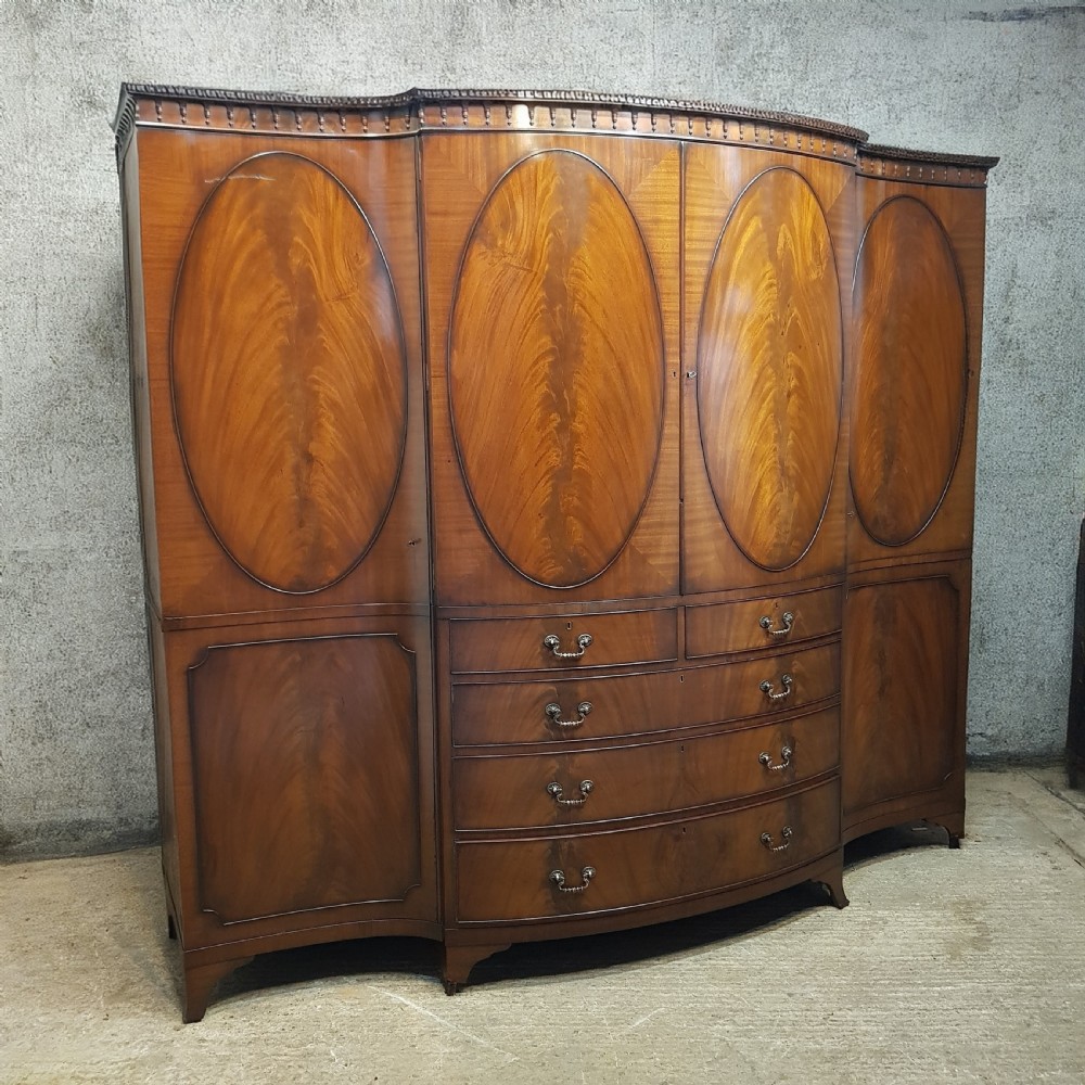 A large mahogany breakfront triple wardrobe featuring oval flame mahogany veneer panels on the doors and a central chest of drawers. View X