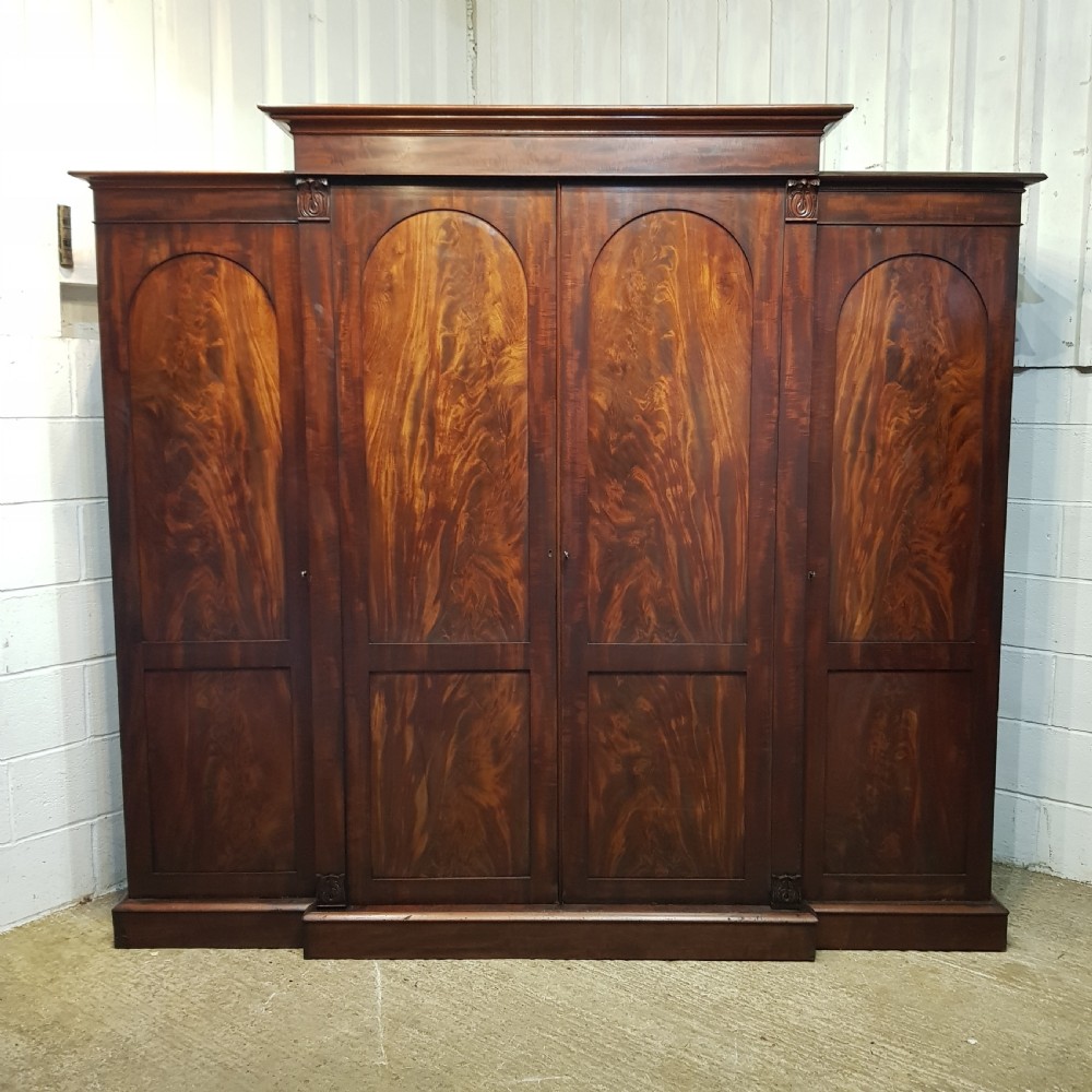 A large mahogany breakfront triple wardrobe featuring oval flame mahogany veneer panels on the doors and a central chest of drawers. View XI