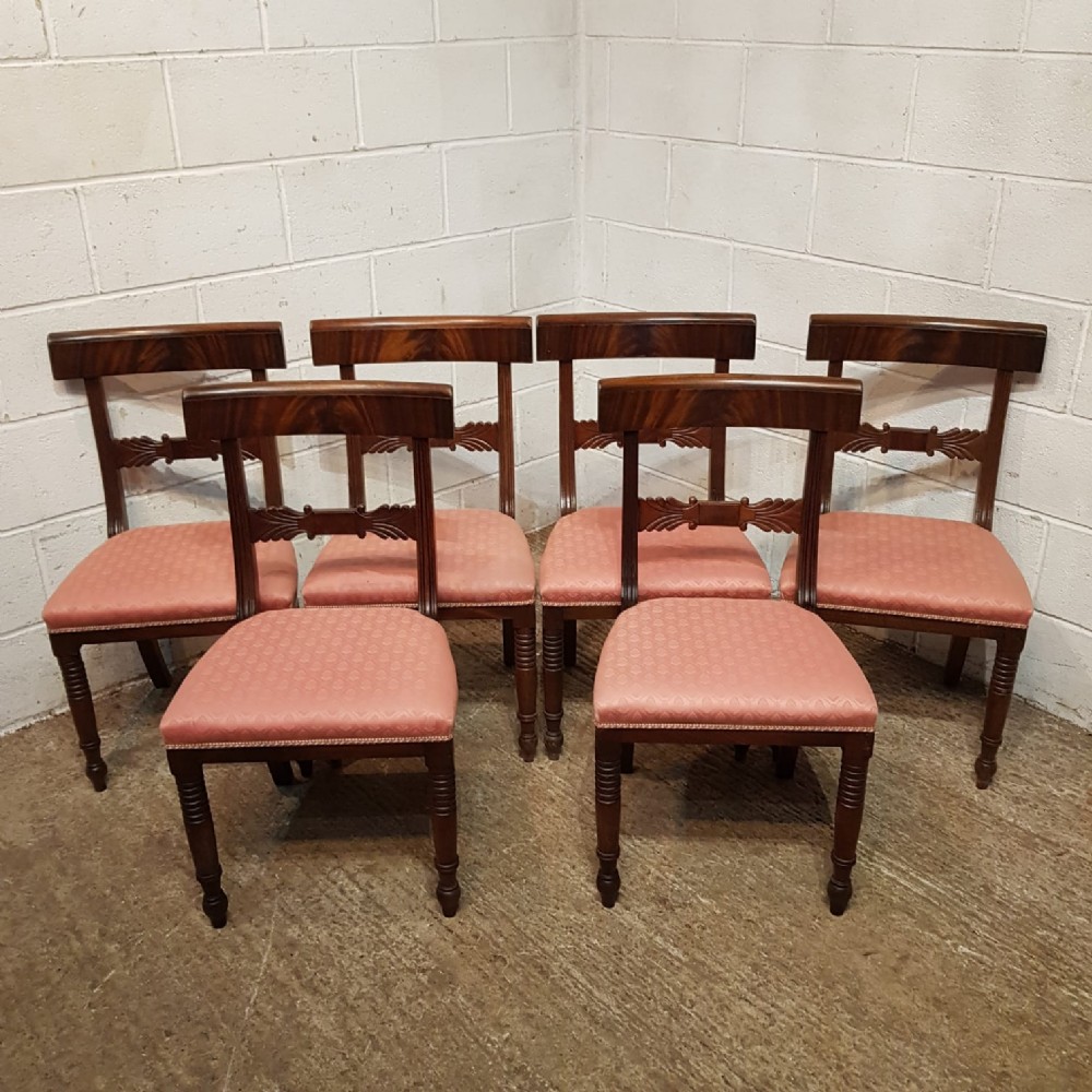 A set of six Regency mahogany dining chairs featuring tablet top rails, carved central splats, dusty pink patterned upholstery, and turned reeded front legs.