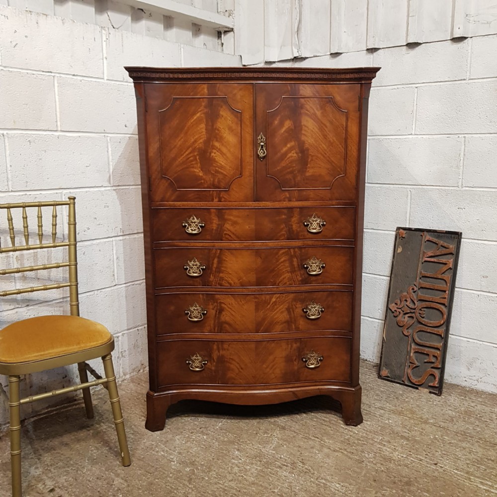 A mahogany Chippendale style tallboy featuring upper cupboard doors with shaped moulding over four serpentine-front drawers with brass handles.