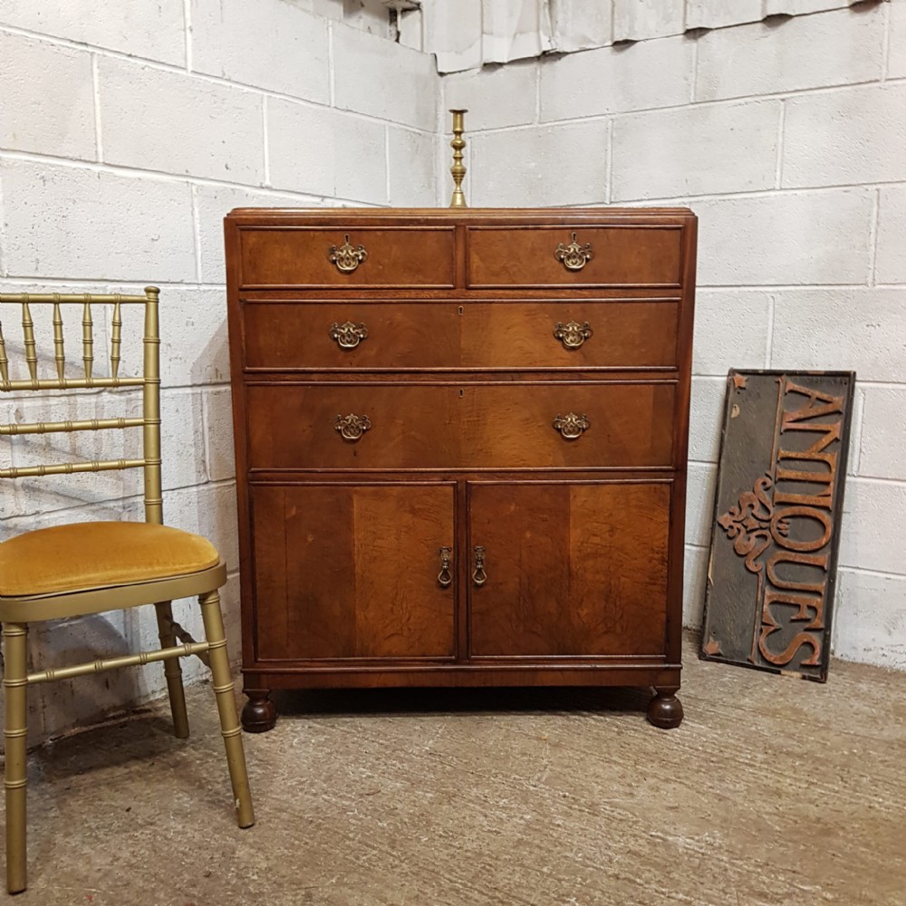 A 1920s burr walnut tallboy featuring three upper drawers with brass handles above a double-door cupboard on turned feet.