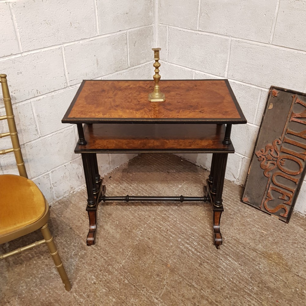 A late Victorian two-tier etagere table with burr walnut tops, ebonised turned legs, beaded brass edging, and an H-stretcher base.