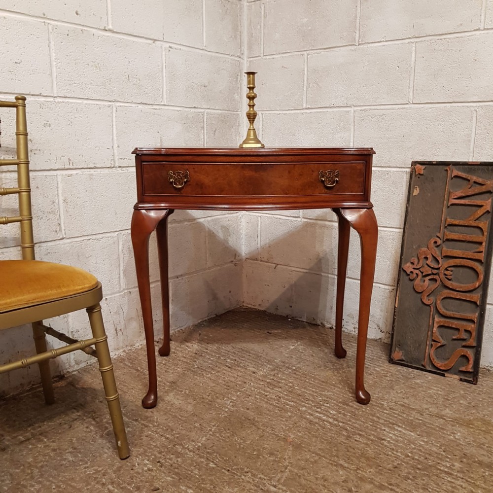 A small burr walnut side table featuring a serpentine-fronted drawer with brass handles, resting on slender cabriole legs.