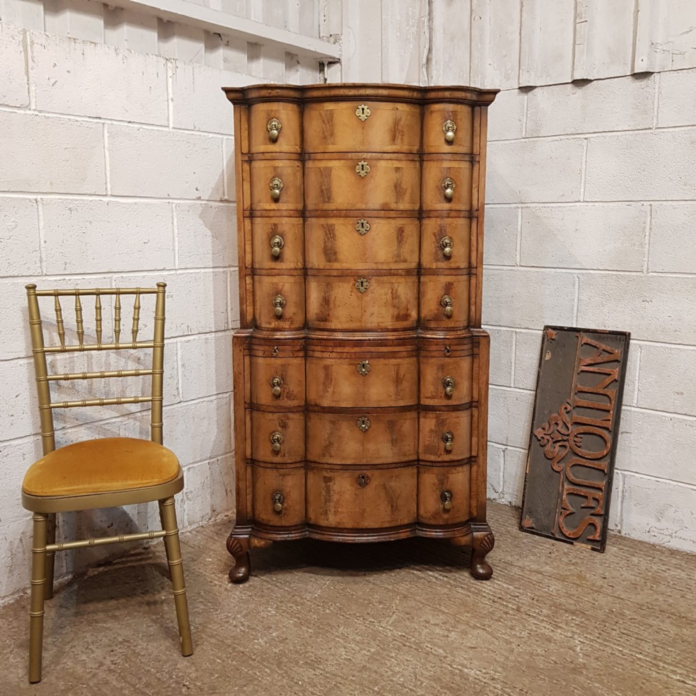A tall Queen Anne style burr walnut chest on chest with a serpentine front, brass drop handles, and cabriole legs.
