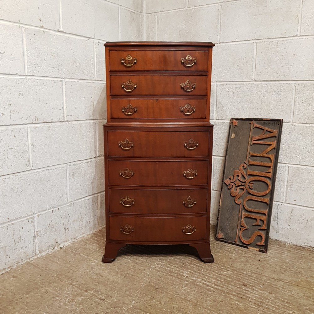 A bow-fronted mahogany dwarf chest on chest featuring seven drawers with brass handles and bracket feet.