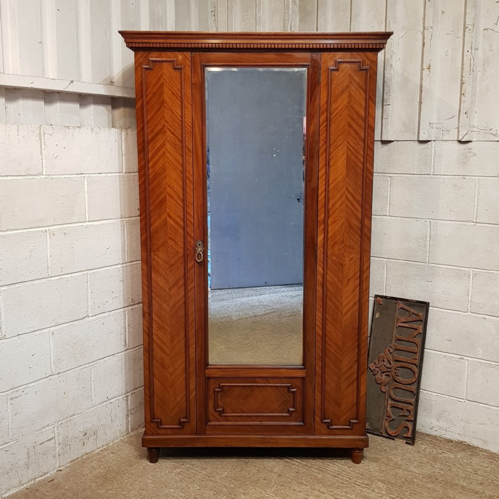 A late Victorian mahogany single door wardrobe featuring a central mirrored panel flanked by chevron-veneered wood sections and topped with a moulded cornice.