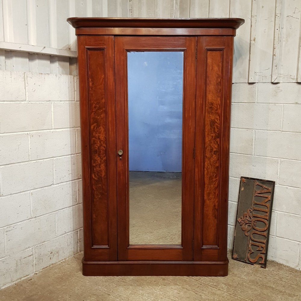 A late Victorian single door mahogany wardrobe featuring a central mirrored door flanked by flame mahogany panels under a moulded cornice.