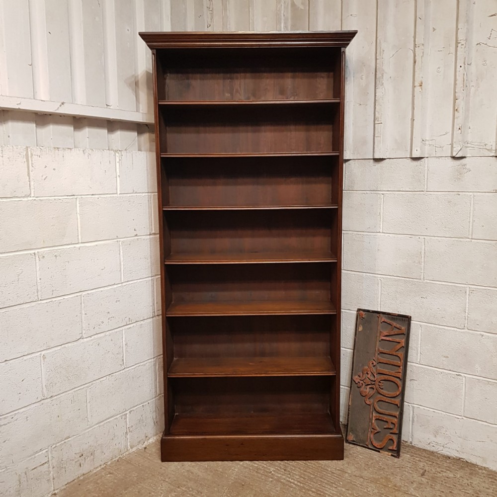A tall Edwardian dark oak open bookcase featuring eight fixed shelves, a top moulded cornice, and a sturdy plinth base.