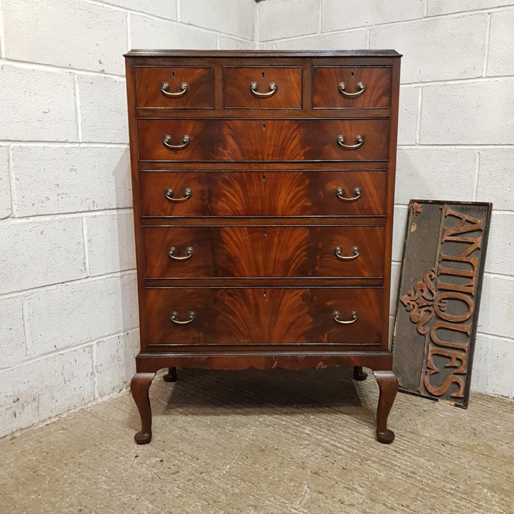 A tall mahogany chest of drawers featuring flame mahogany veneer fronts, brass drop handles, and cabriole legs.