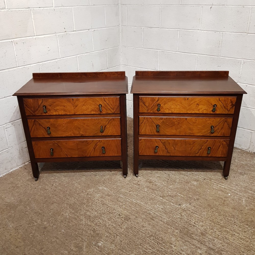 A matching pair of three-drawer chests crafted from walnut with prominent burr walnut veneer drawer fronts and low gallery backs.