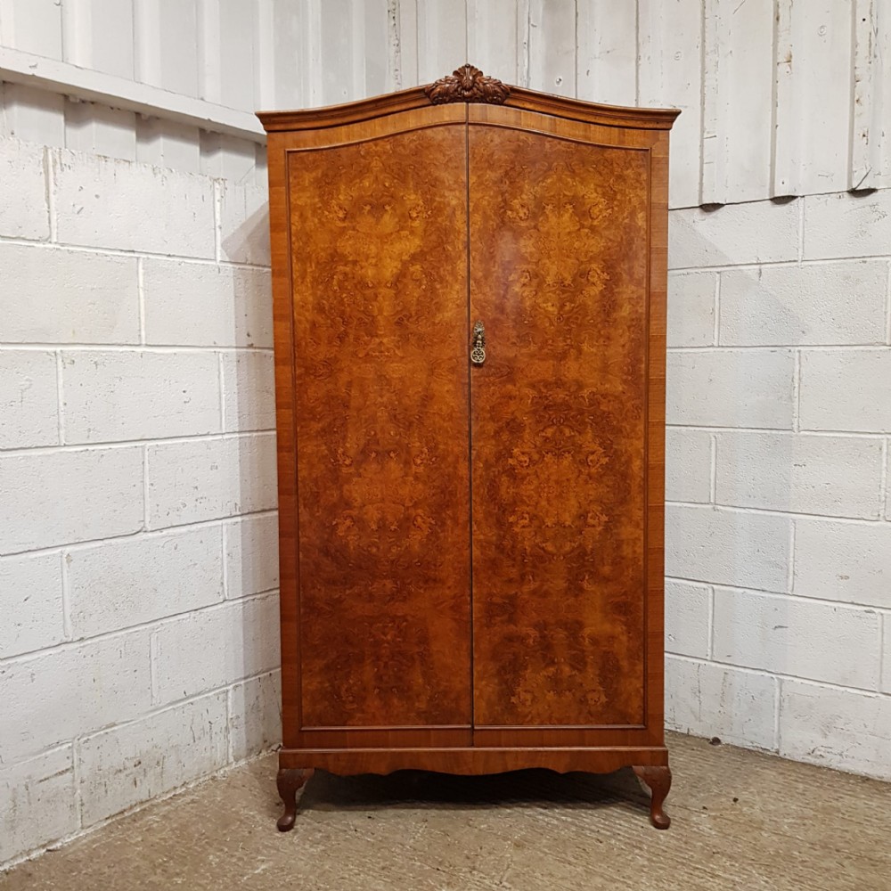 A small 1920s burr walnut fitted wardrobe featuring double doors with book-matched grain, a carved top crest, and short cabriole legs.