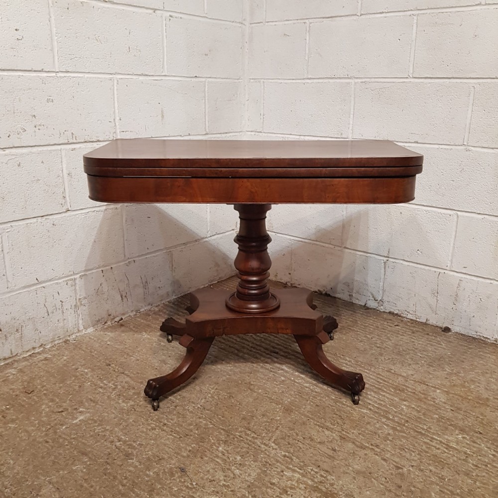A Regency mahogany fold-over table featuring a rounded rectangular hinged top on a central turned pedestal column with four splayed legs and brass castors.