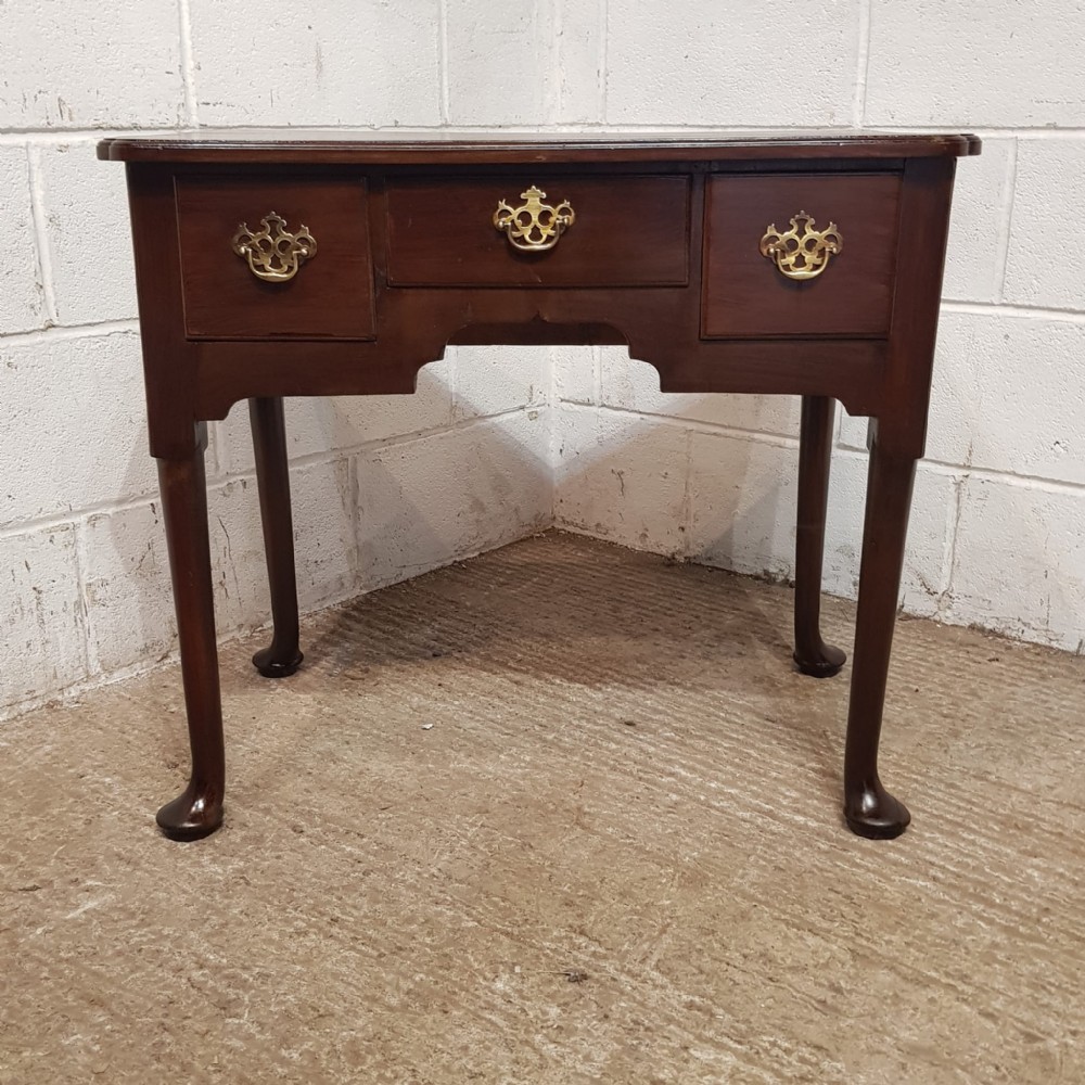 A George III dark mahogany lowboy featuring three drawers with brass handles, a shaped apron, and cabriole legs terminating in pad feet.