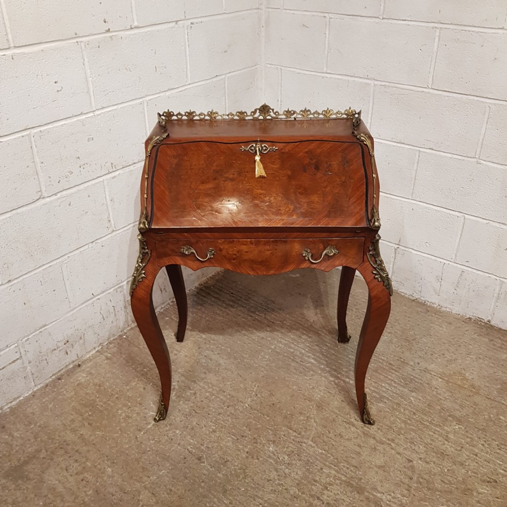A French Louis XV style walnut bureau de dame featuring cabriole legs, a slant-front lid with brass key tassel, decorative brass mounts, and a pierced top gallery.