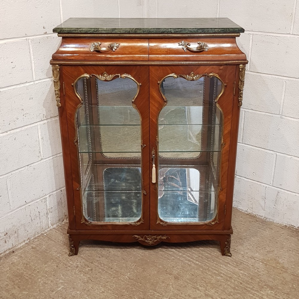 A walnut vitrine cabinet featuring shaped glazed doors, gilt metal mounts, a green marble top, and a mirrored back interior.