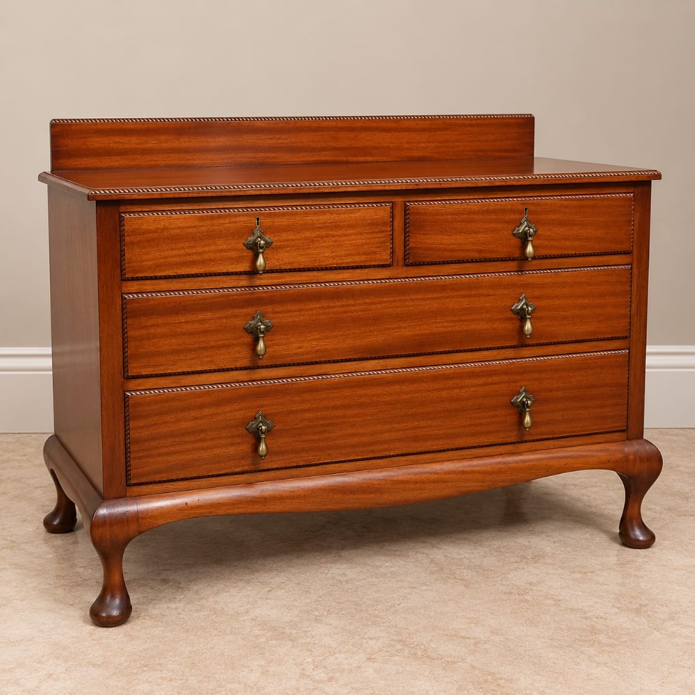 An Edwardian mahogany chest of drawers featuring two short over two long drawers, brass drop handles, a low gallery back, and cabriole legs.