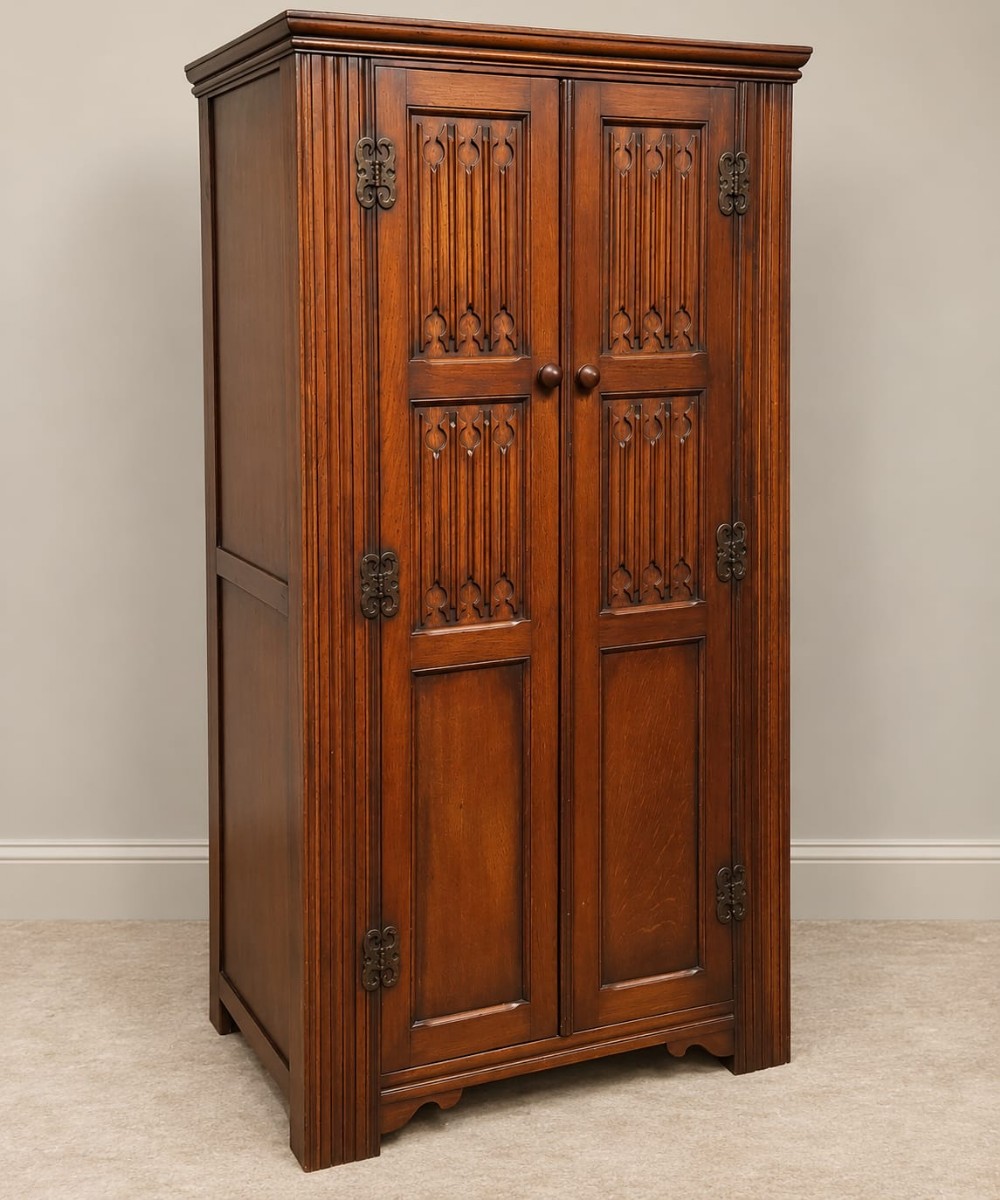 A small 1920s oak double wardrobe featuring carved gothic tracery panels, reeded corner pilasters, decorative iron hinges, and a moulded top cornice.