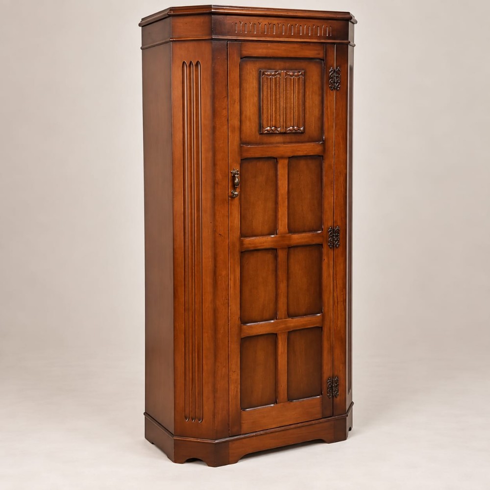 A tall brown oak hall wardrobe with a single panelled door featuring carved details, fluted canted corners, and iron hardware.