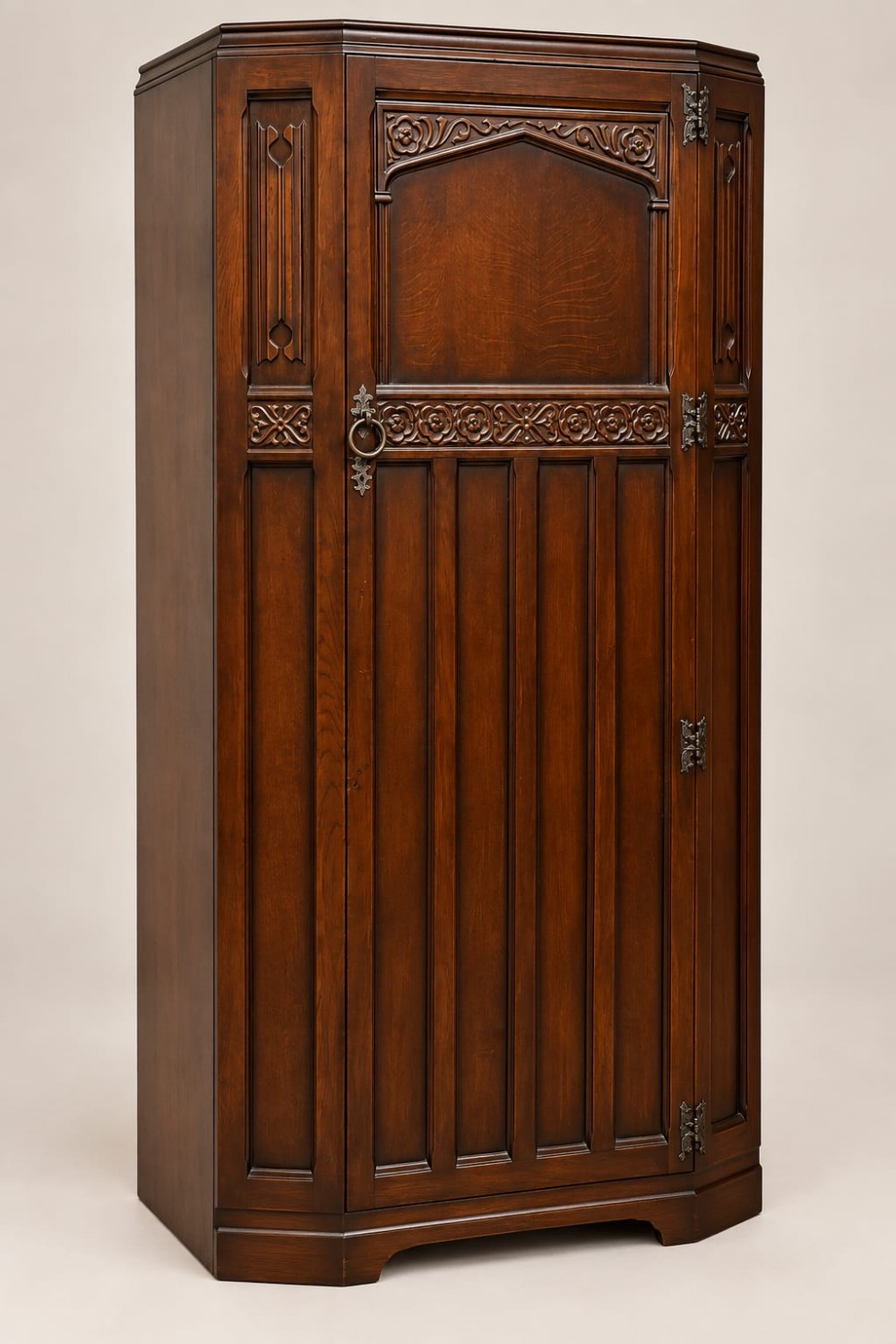 A dark oak single-door wardrobe featuring carved floral band detailing, an arched upper panel, vertical linear panelling, and iron hardware.