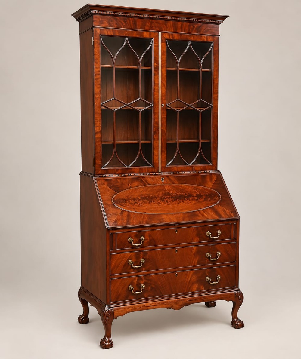 An Edwardian Chippendale Revival mahogany bureau bookcase featuring an upper glazed cabinet, slant-front writing desk with flame mahogany oval inlay, lower drawers, and cabriole legs with ball-and-claw feet.
