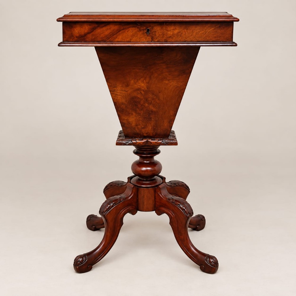 A Victorian burr walnut work table featuring a hinged rectangular top, conical trumpet well, turned central column, and four carved cabriole legs.