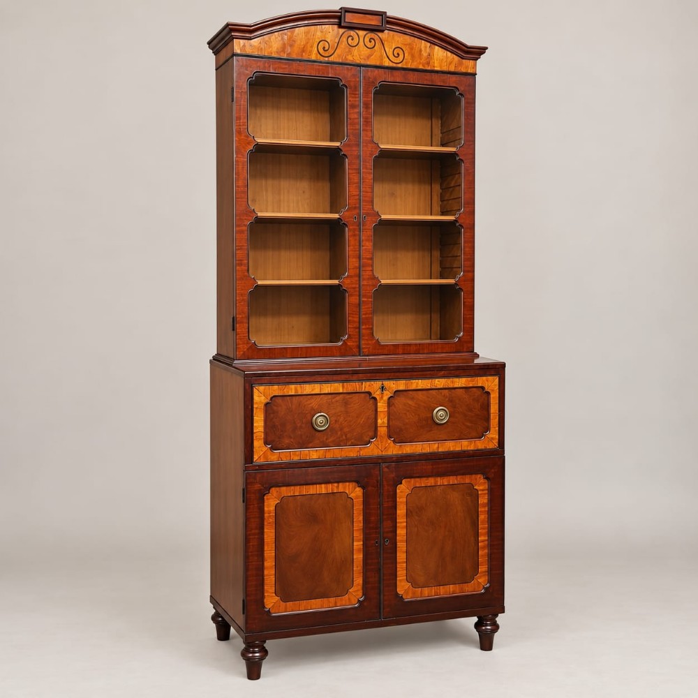 A George III mahogany and satinwood crossbanded secretaire bookcase featuring a glazed upper section, a pull-down writing drawer, two lower cupboard doors, and turned feet.