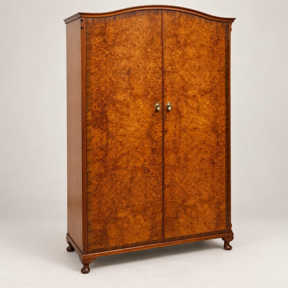 A 1920s double wardrobe crafted from burr walnut featuring an arched cornice, twin doors with brass hardware, and turned feet.