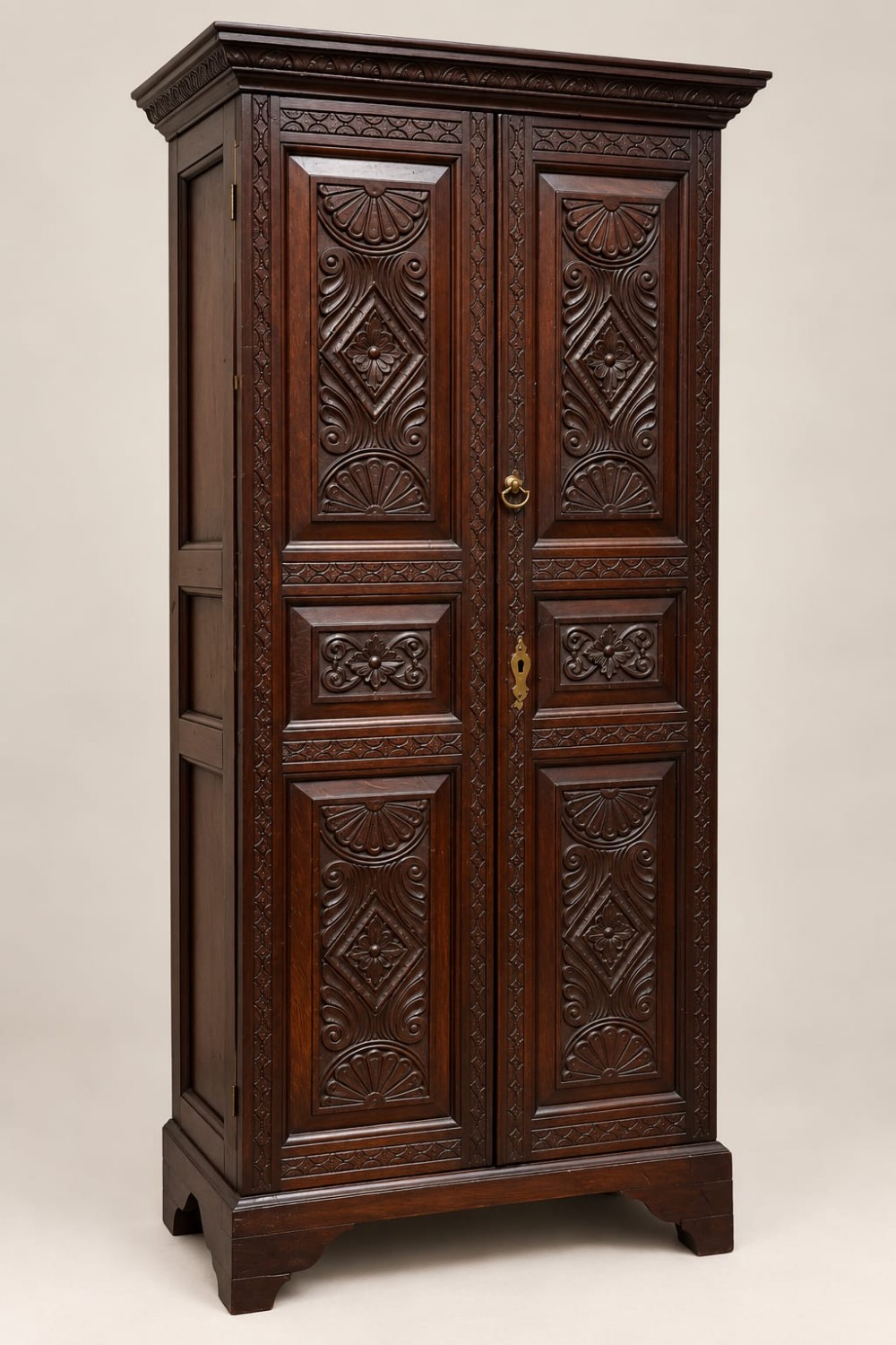 A tall dark oak George III cupboard featuring two panelled doors decorated with carved lunettes, rosettes, and geometric motifs, standing on bracket feet.