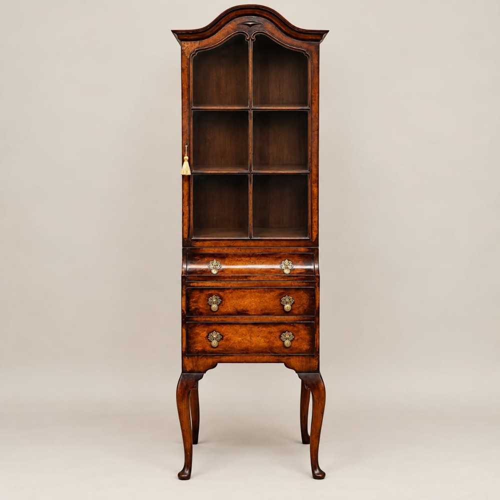 A tall, narrow burr walnut cabinet featuring an arched glazed upper section above three drawers supported by slender cabriole legs.