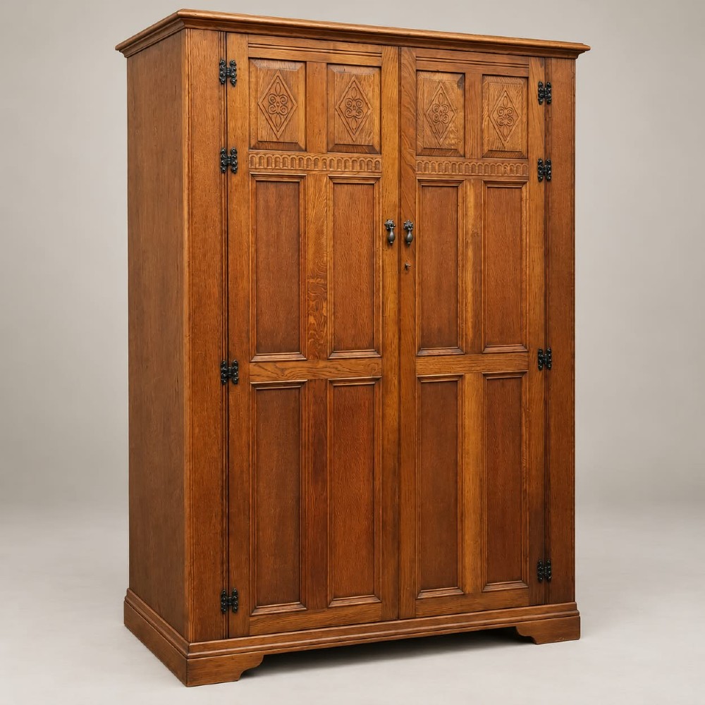 A two-door warm brown oak wardrobe featuring carved diamond motifs on upper panels, recessed rectangular lower panels, and dark iron hardware.
