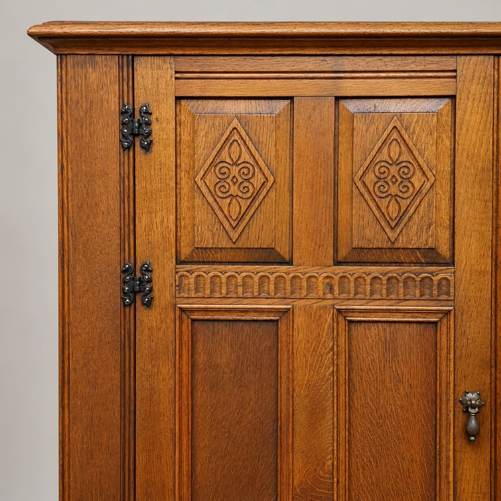 A two-door warm brown oak wardrobe featuring carved diamond motifs on upper panels, recessed rectangular lower panels, and dark iron hardware. View V