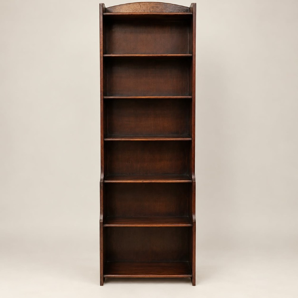 A tall and narrow dark oak waterfall bookcase circa 1920 with six open shelves graduating in depth.