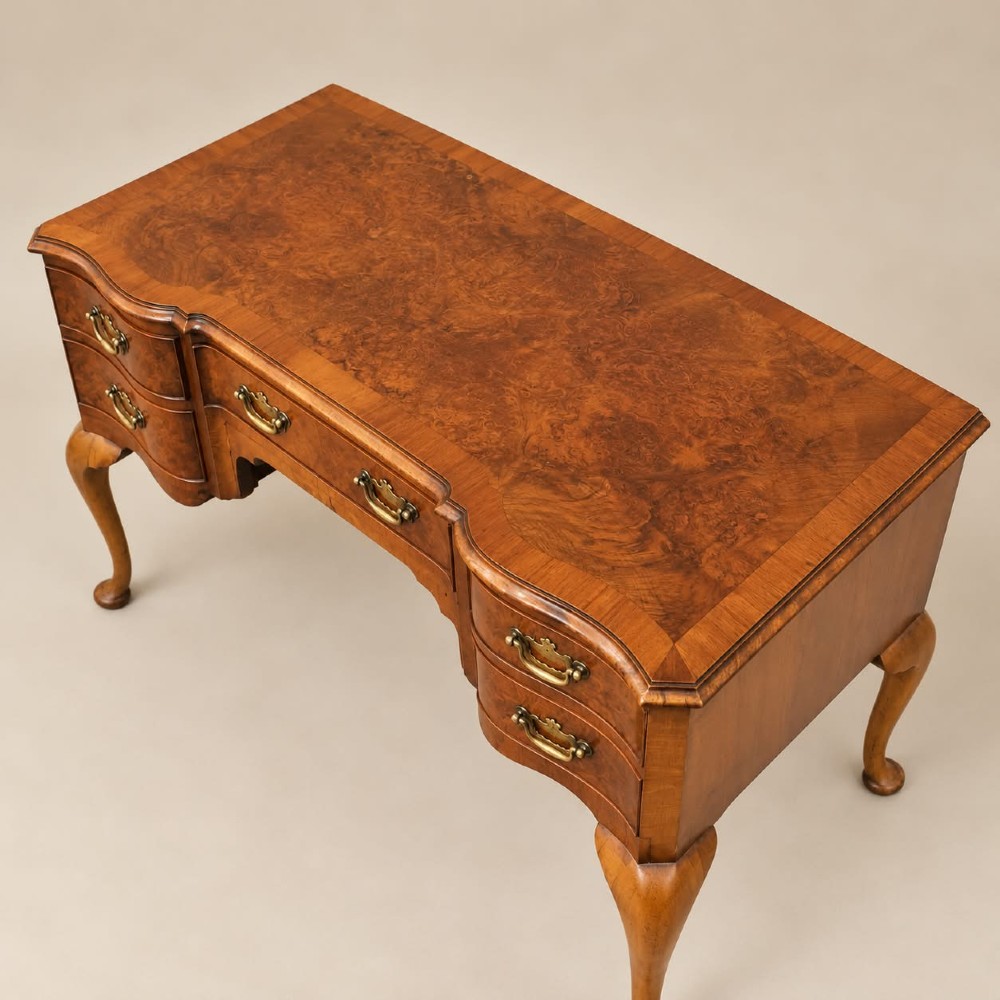 A 1920s burr walnut serpentine-fronted desk featuring five drawers with brass handles and cabriole legs. View V