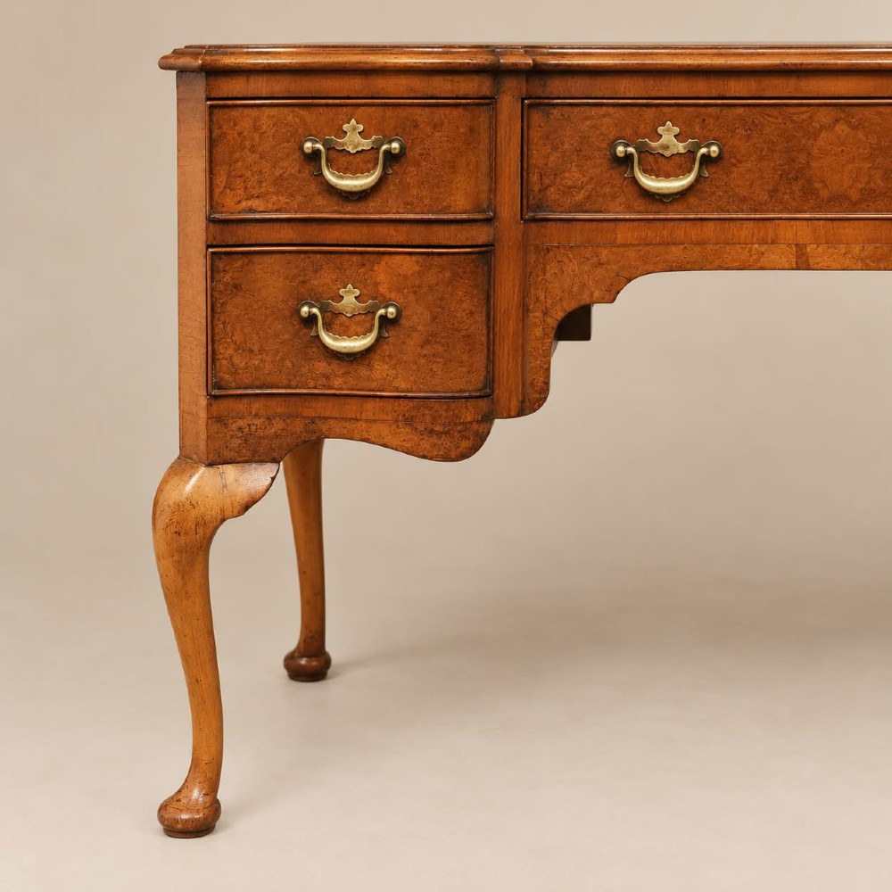 A 1920s burr walnut serpentine-fronted desk featuring five drawers with brass handles and cabriole legs. View VI