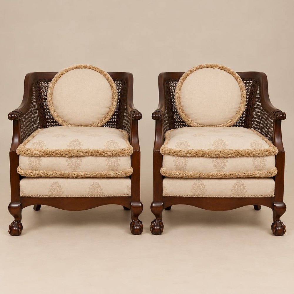 A pair of 1920s mahogany tub chairs featuring woven cane side panels, carved claw and ball feet, and cream upholstered cushions with matching circular accent pillows.