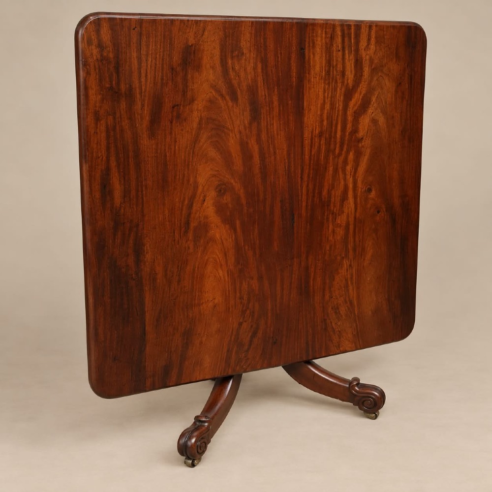 A late Georgian mahogany tilt-top dining table featuring a central turned pedestal and splayed quadform legs with brass castors. View IV