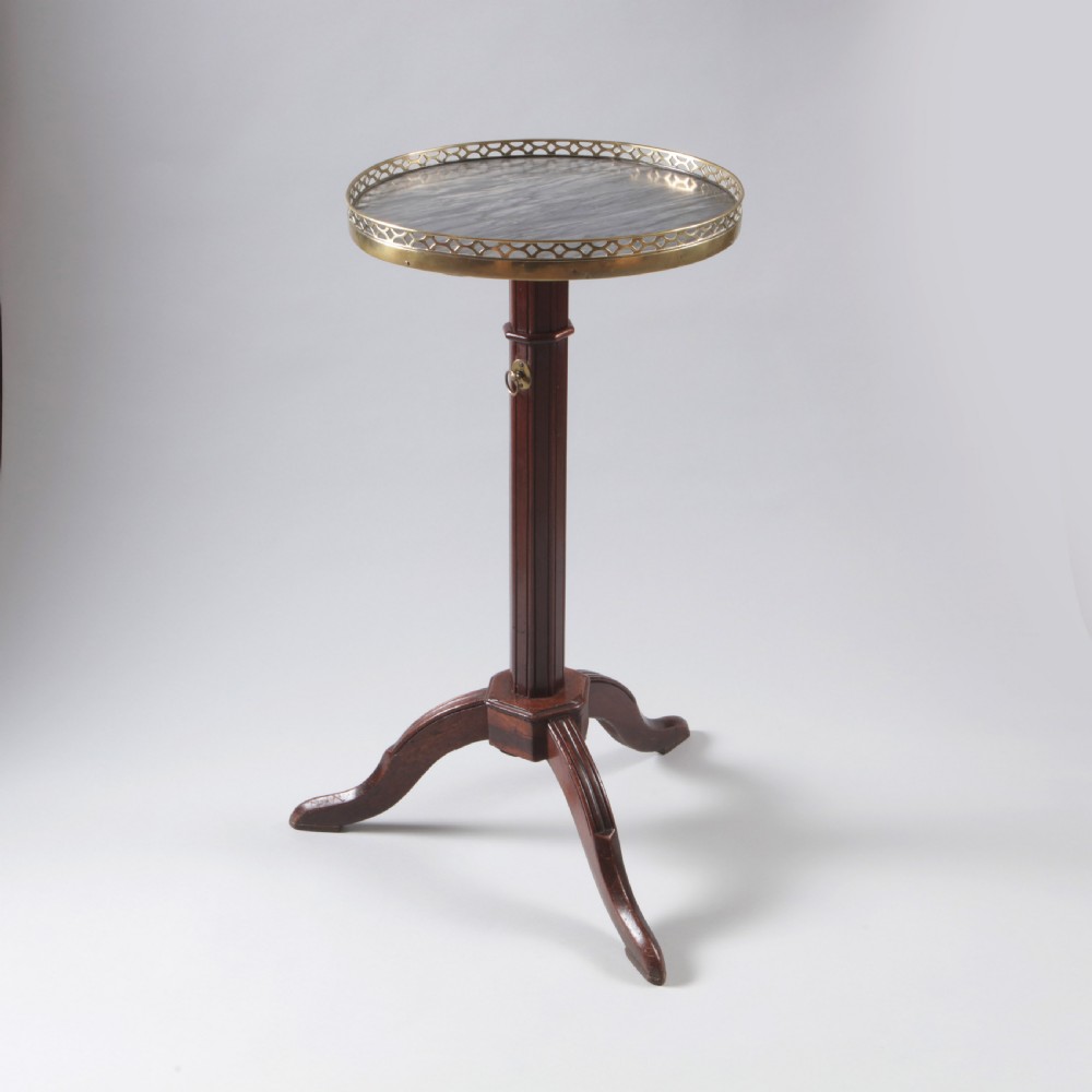 A Louis XVI style mahogany wine table featuring a circular grey marble top enclosed by a pierced brass gallery, supported on a fluted central pedestal and tripod legs.