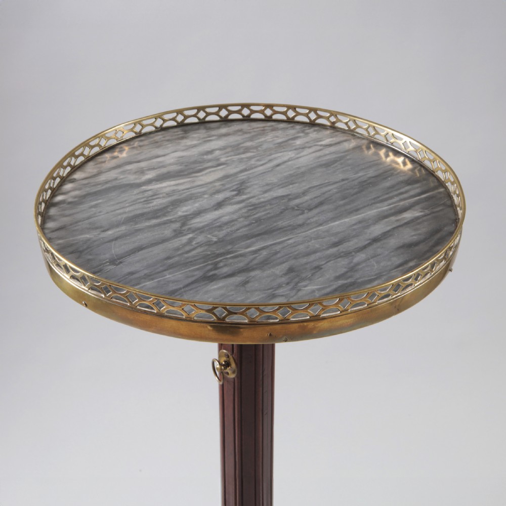 A Louis XVI style mahogany wine table featuring a circular grey marble top enclosed by a pierced brass gallery, supported on a fluted central pedestal and tripod legs. View II